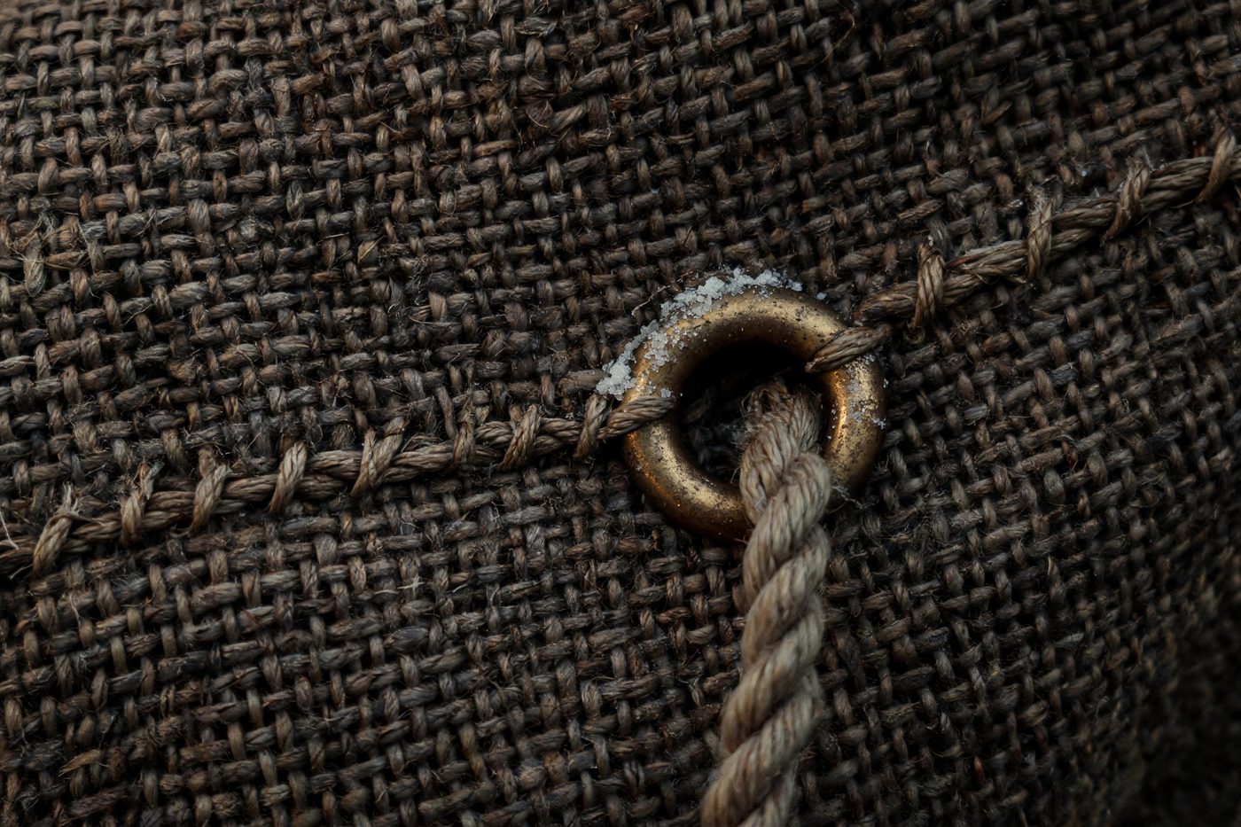 Close detail of heavy sailcloth, a stitched seam and a brass eyelet with rope
